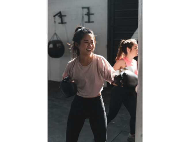 A woman in pink long sleeve shirt and black pants wearing black boxing gloves practicing martial arts for women.