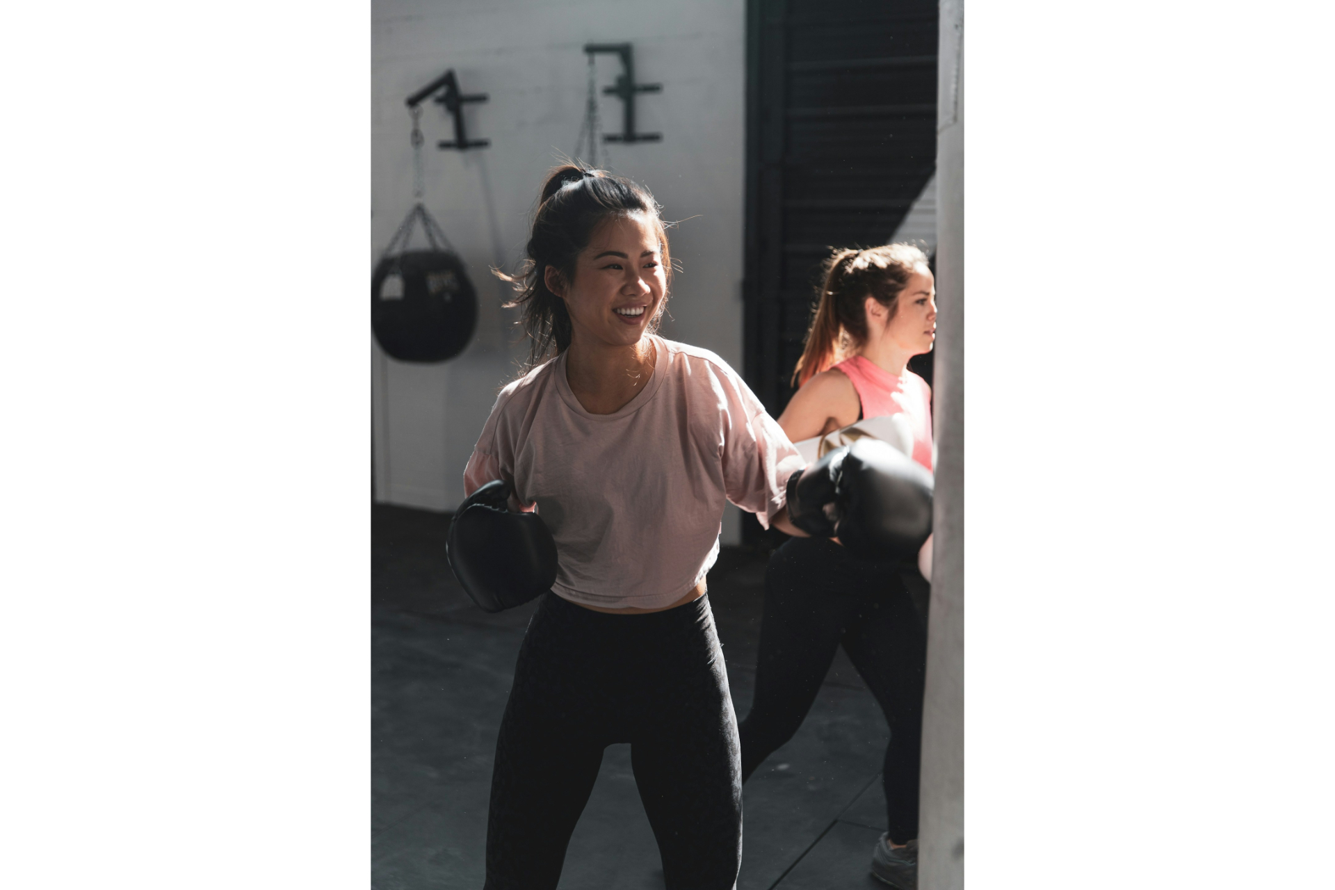 A woman in pink long sleeve shirt and black pants wearing black boxing gloves practicing martial arts for women.