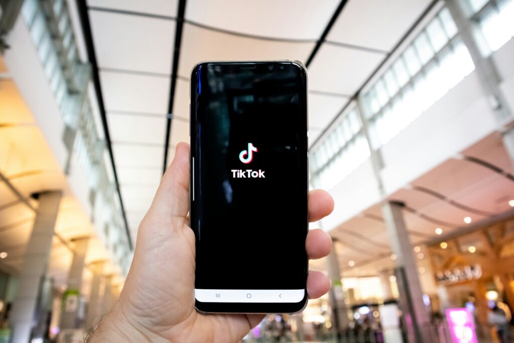 A person holds up their smart phone in a mall. The screen is the TikTok loading screen.