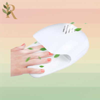 A small white pressure-activated nail dryer sits against the Revivalist branded background of pink, orange, yellow and green stripes. A person's hand sits on the pressure plate so the fan dries their orange-peach polish.