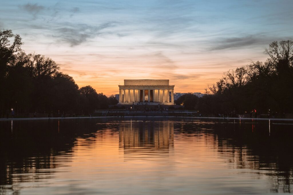 The Lincoln Memorial sits under a sunset. The reflecting pool is in front of it. 