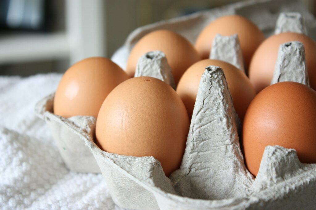 An open carton of brown eggs sits on a white towel in the sunshine.
