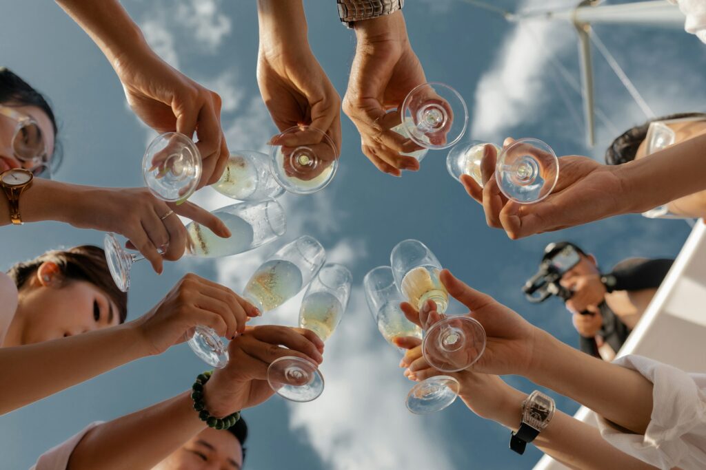 A group of friends clink champagne glasses under a cloudy blue sky.