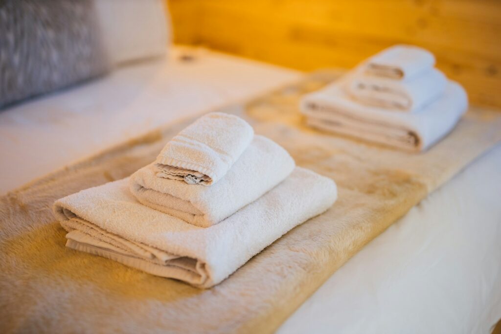 Two small piles of folded white towels sit on a white bed. They may have lavender oil scents based on the latest Meghan Markle quotes from her Netflix show about hosting.