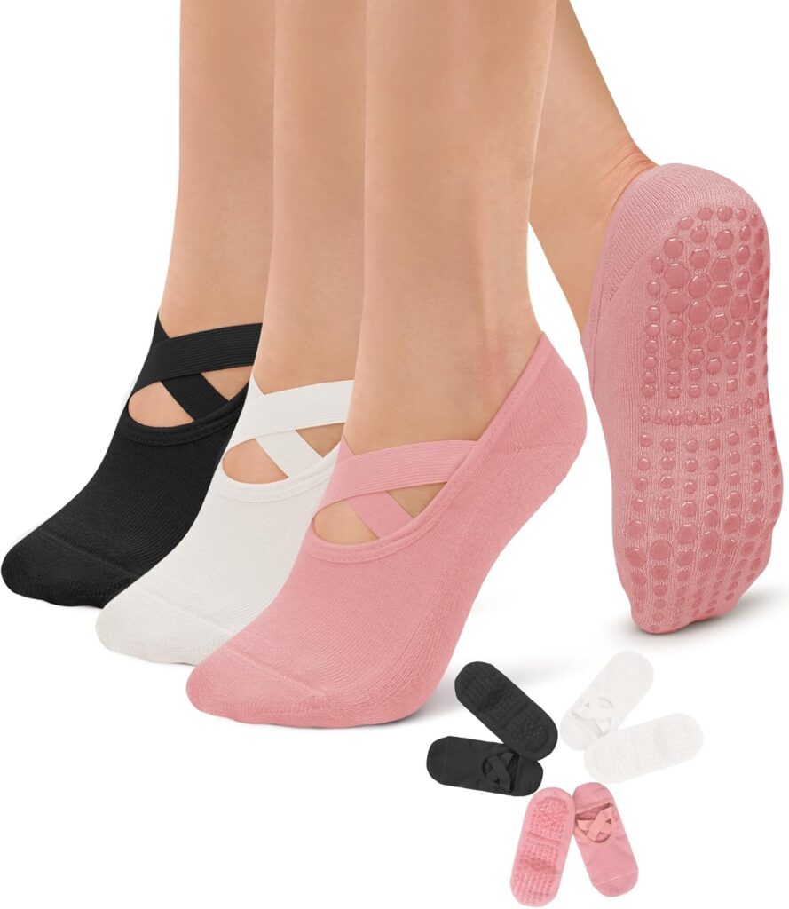 Three women stand in ballerina shoe shaped grippy socks. One pair is black, one is white, and the other is pink. Another set of matching socks without feet in them are arranged in a circle beneath.