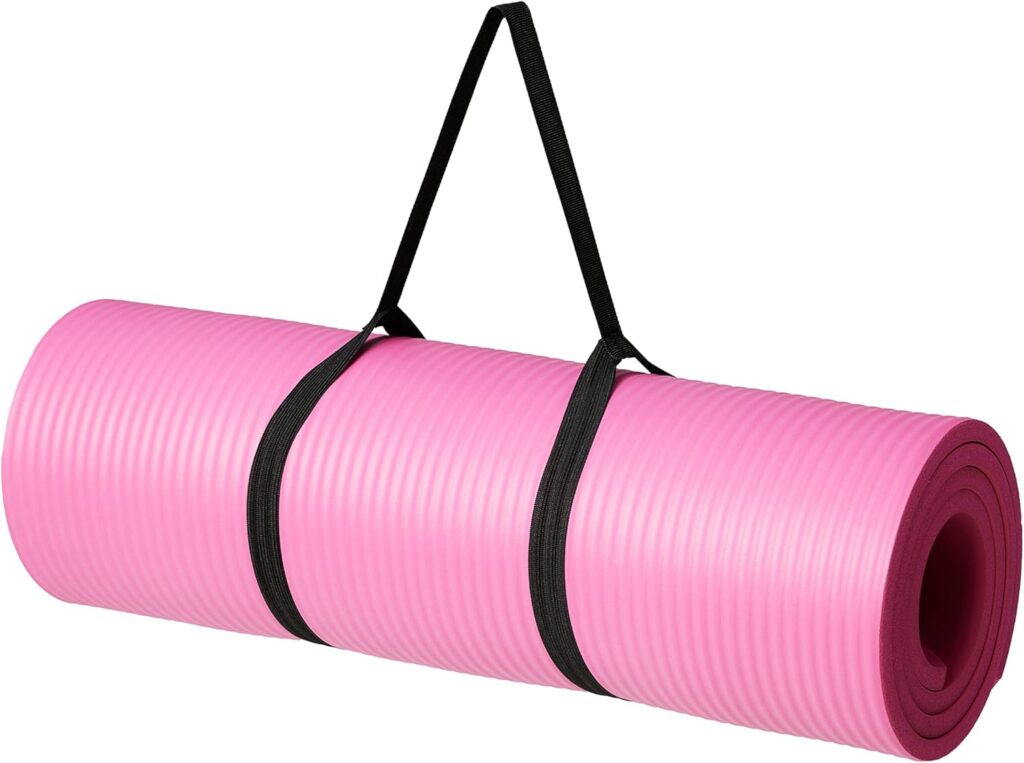 A pink yoga mat sits against a white background, rolled up in a black carrying strap.